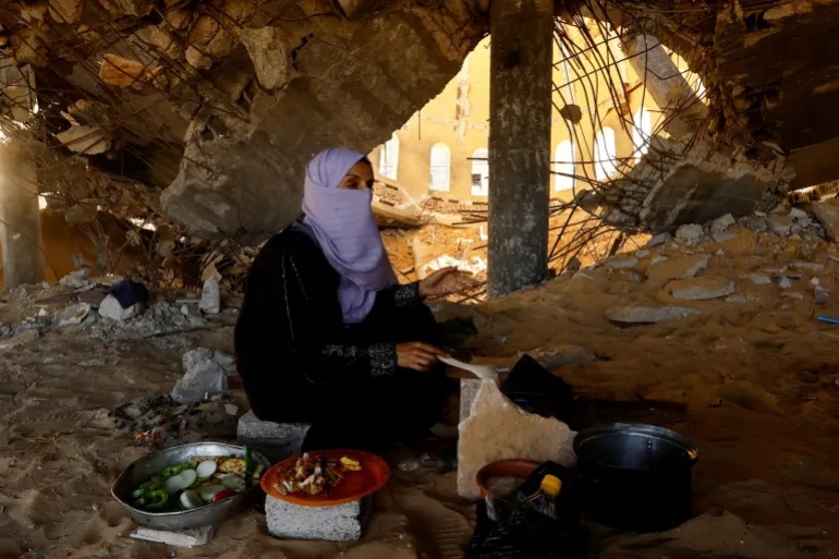 سيدة فسلطينية تعد الطعام تحت أنقاض أحد المساجد التي طالها القصف الإسرائيلي (رويترز)